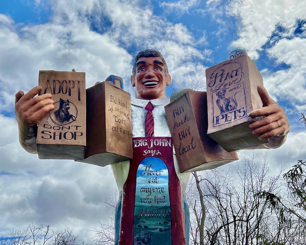 large statue of man carrying grocery bags with animal-friendly messages