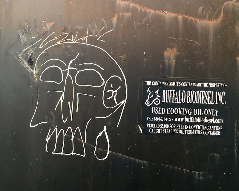 crude graffiti drawing of a skull on the outside of a dumpster
