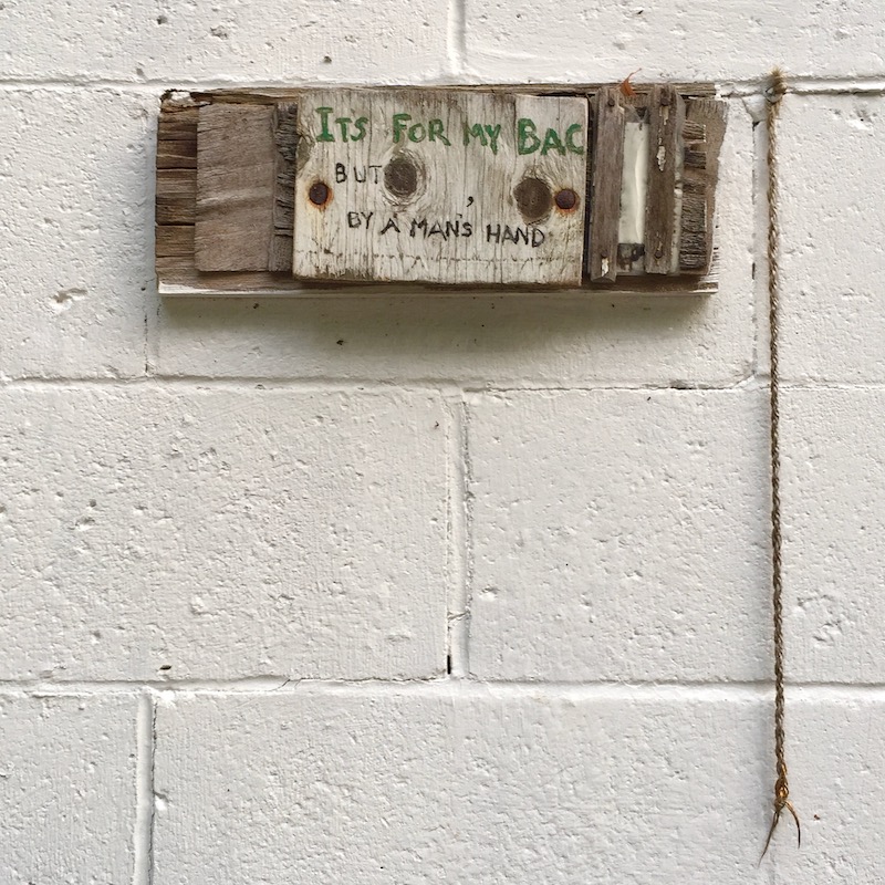 small sign on cinderblock wall reading "It's for my bac... but by a man's hand."