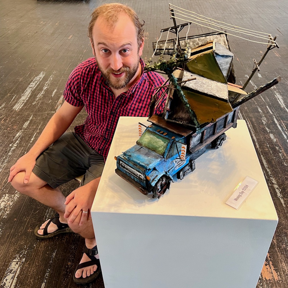 Artist Nathan Van Patter with a sculpture of moving truck holding an entire deconstructed house
