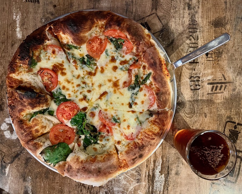 an irregularly-topped pizza on a tabletop with glass of beer