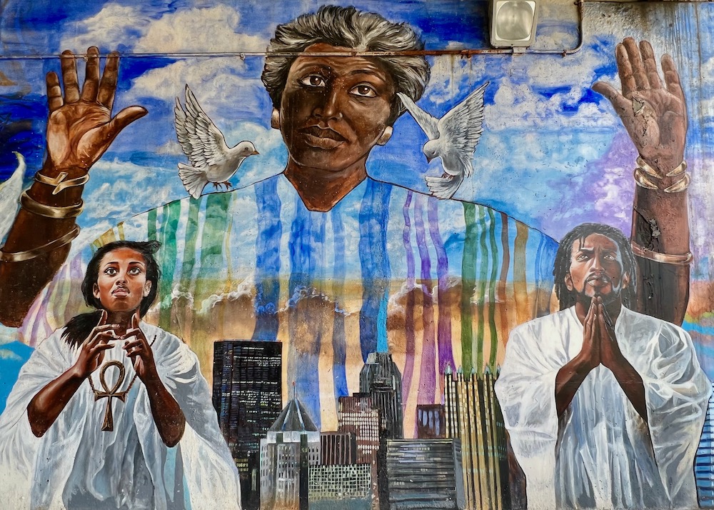 mural of people in vestments praying with skyline of downtown Pittsburgh