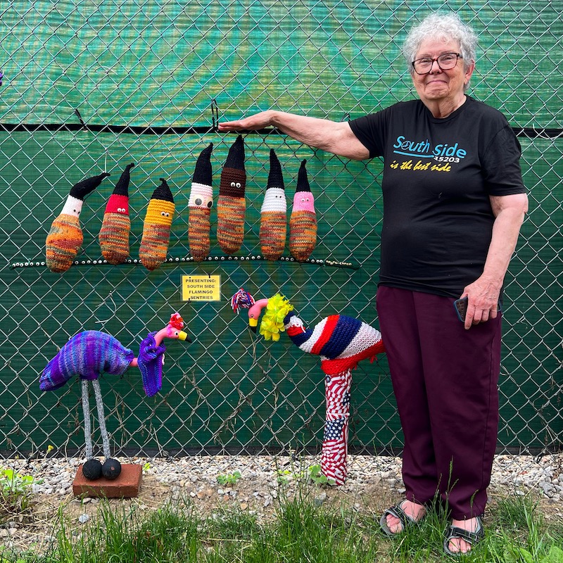 fiber artist Delli Speers with a set of decorations along a public fence