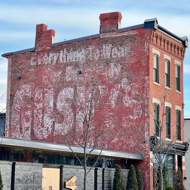 faded hand-painted sign for clothing store painted on brick wall