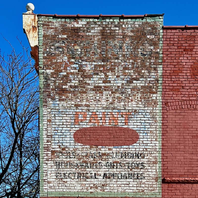 faded hand-painted sign for hardware store painted on brick wall