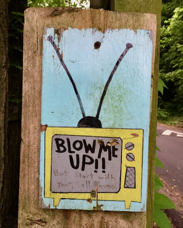 painting of television with message "Blow me up!!" attached to fence