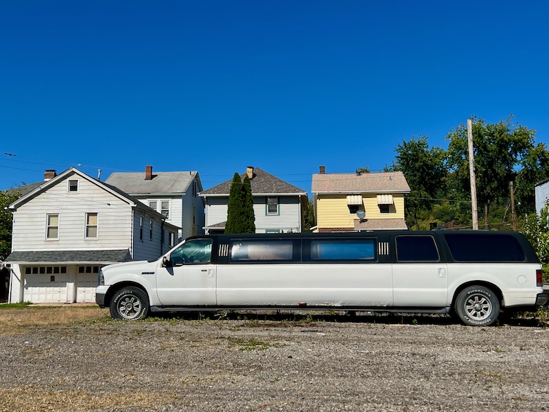 limousine parked in gravel lot by simple frame houses